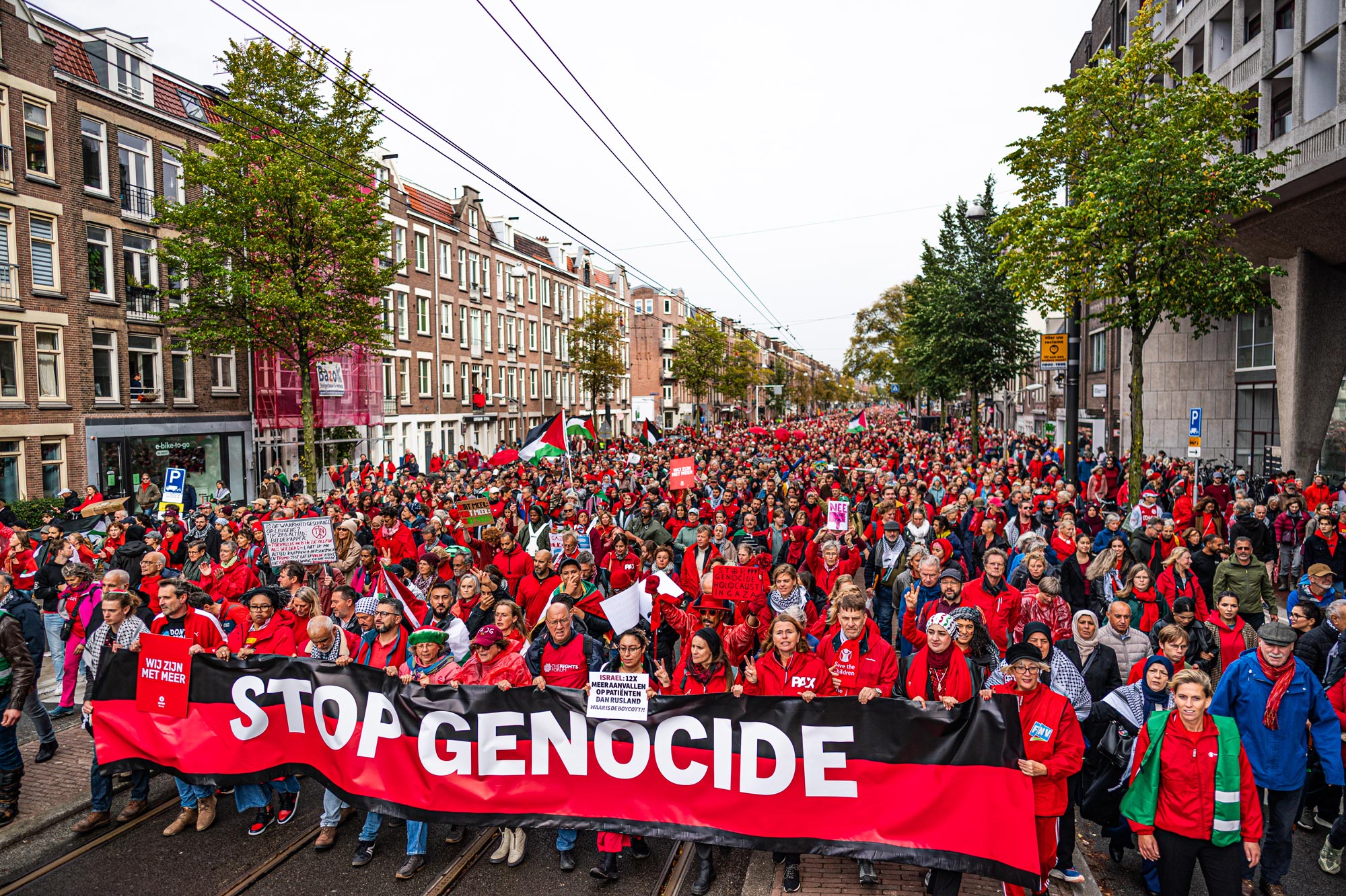 Een lange stoet demonstranten in het rood met Palestijnse vlaggen trekt door een Amsterdamse straat
